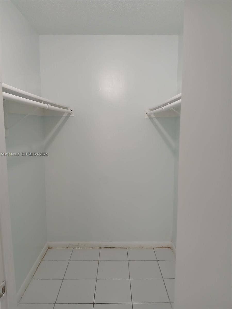 Reach-in storage area featuring white tile flooring and dual-level hanging rods