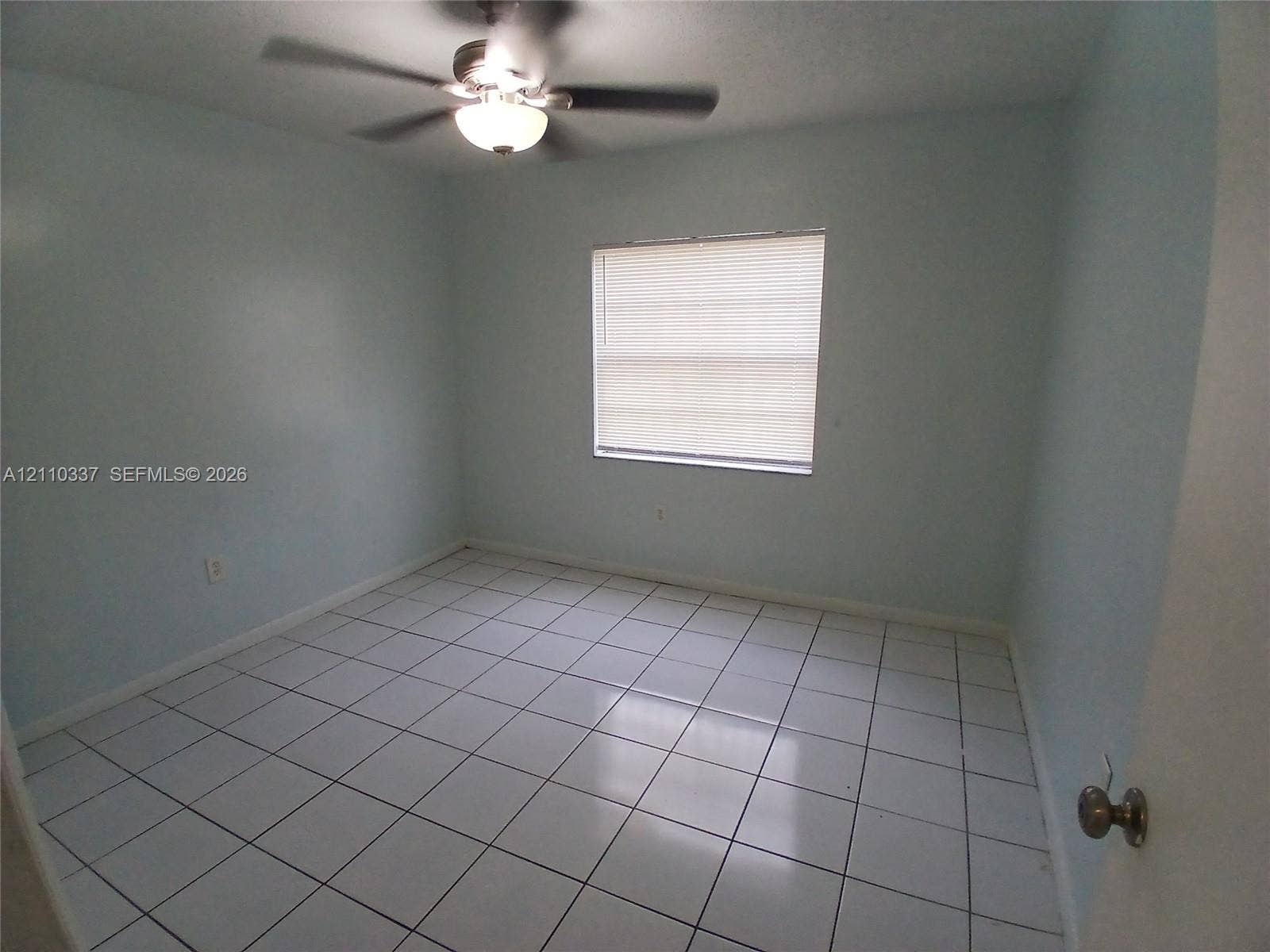 Interior room featuring white tile flooring, neutral wall paint, and a ceiling-mounted light fixture with an integrated fan