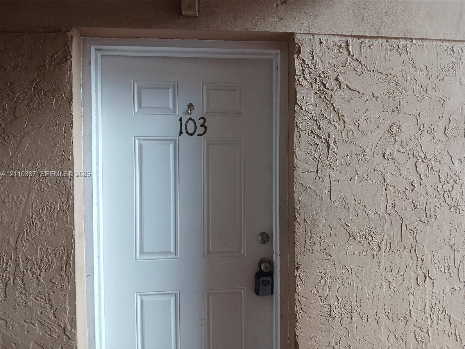 White entry door with a four-panel design and a textured stucco exterior wall