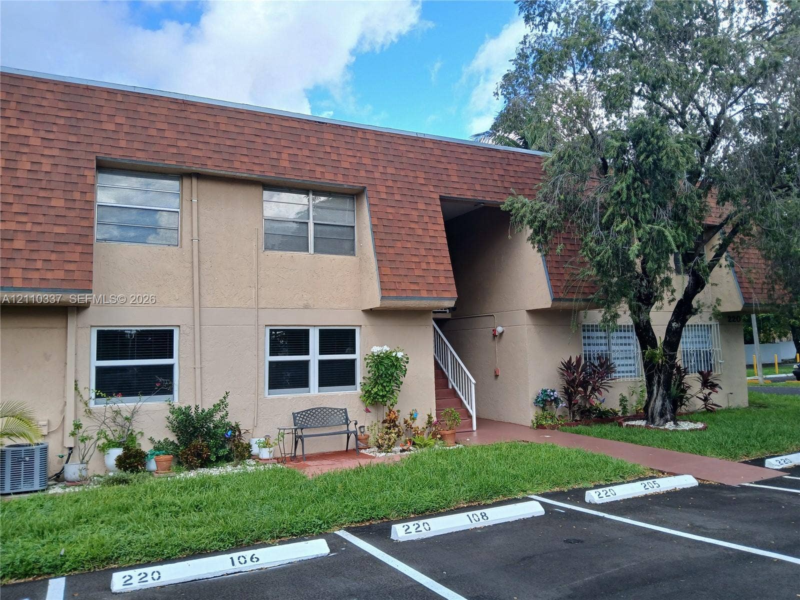 Two-story exterior featuring a mansard roof, stucco facade, sliding windows, and an external staircase with metal railing