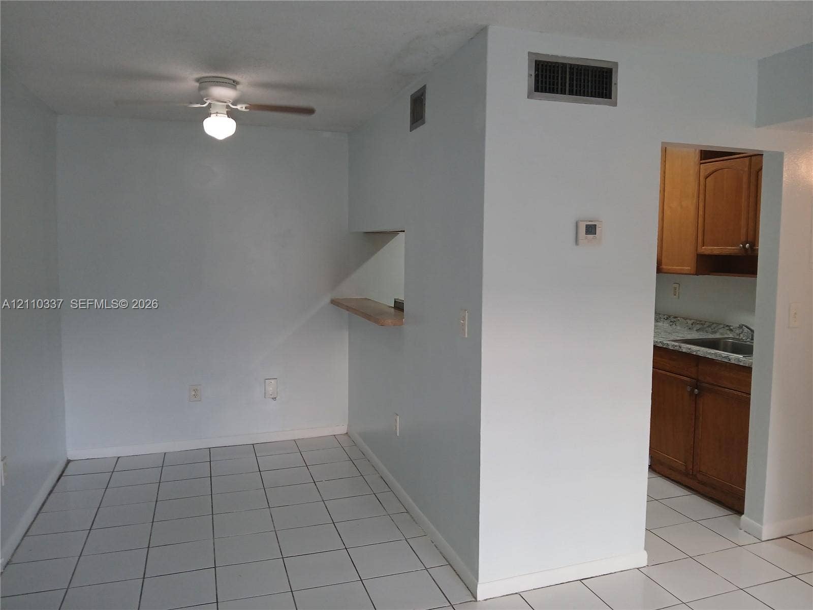 Ceramic tile flooring, white ceiling fan with attached light fixture, and pass-through window with wooden shelf