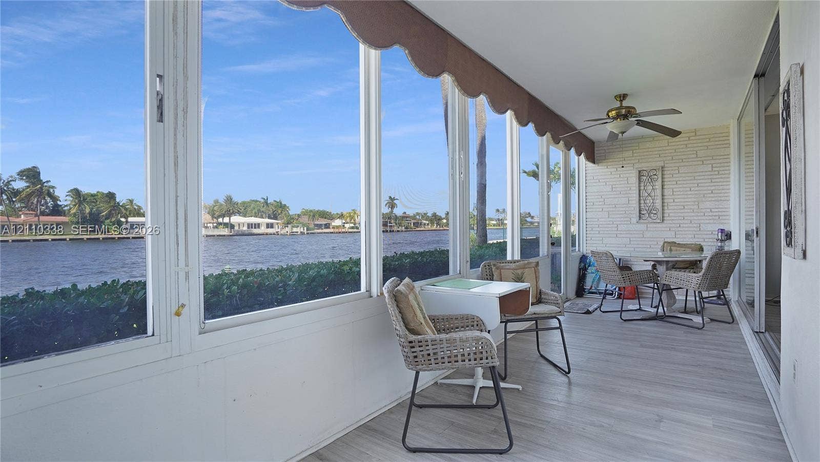 Enclosed lanai featuring full-height glass window walls, painted brick wall finish, wood-finish flooring, and a ceiling fan