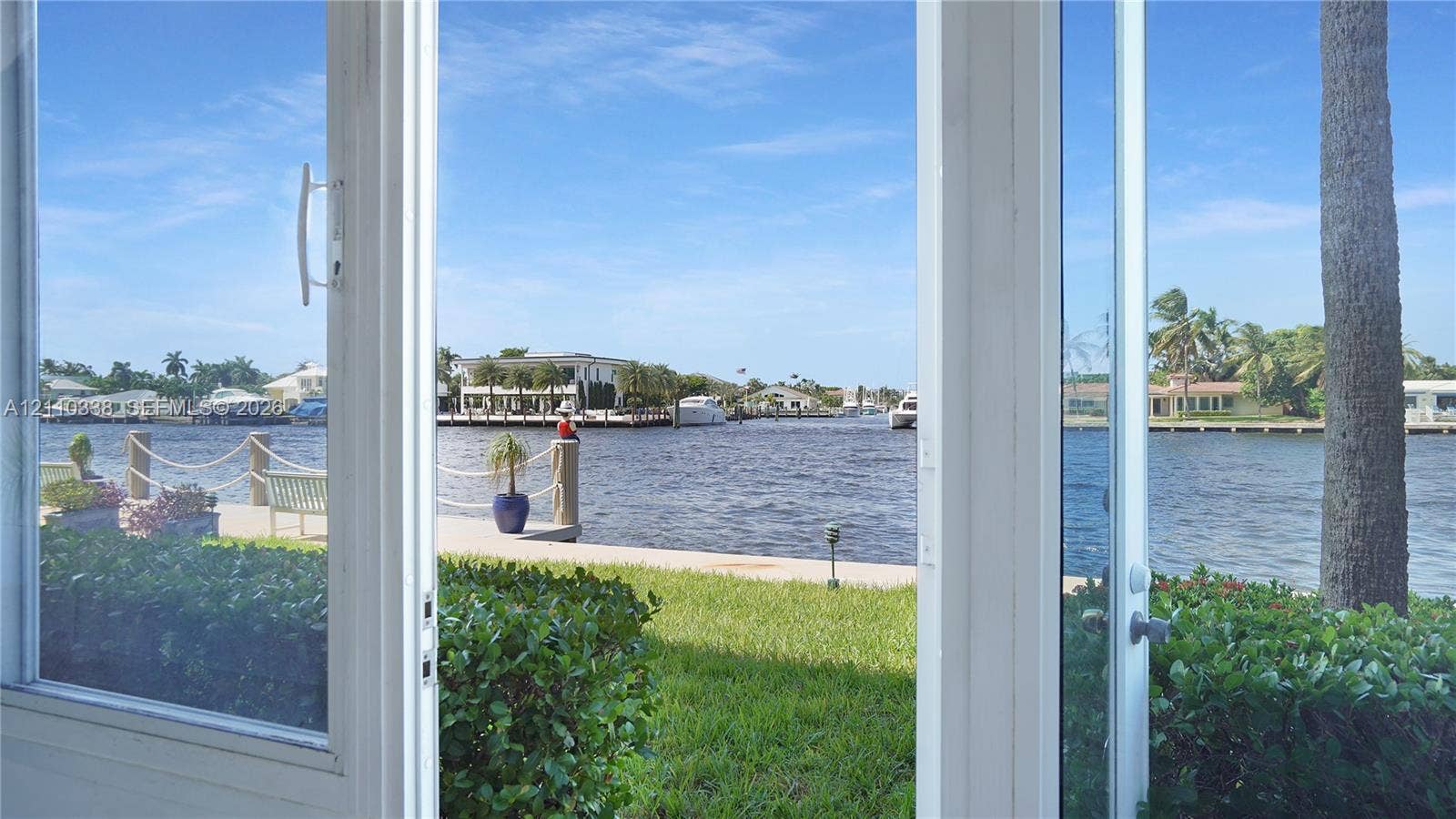 White-framed glass door system, concrete seawall, rope-railing dock, manicured lawn, and waterfront access
