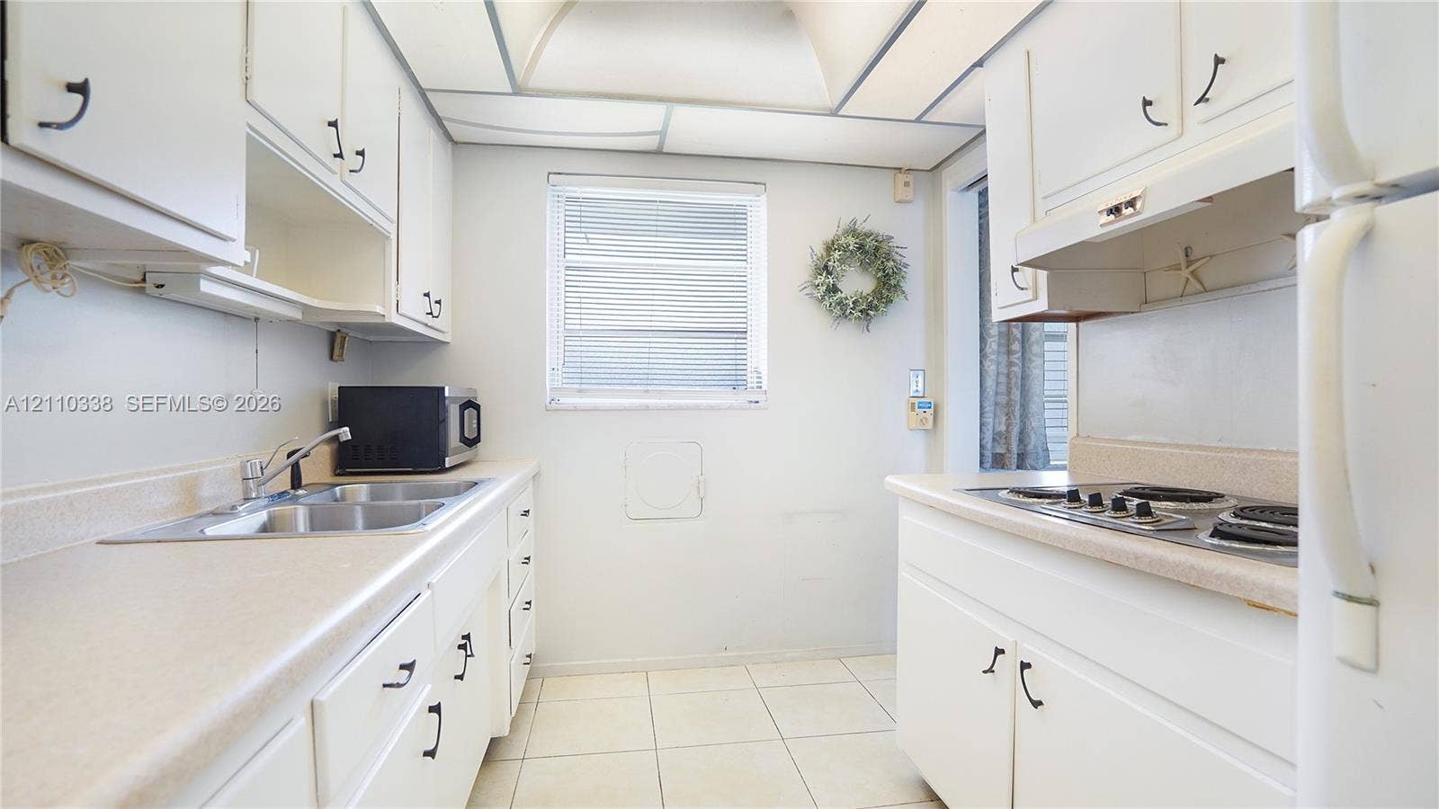 Kitchen featuring white cabinetry, light-toned solid surface countertops, dual-basin stainless steel sink, built-in cooktop, and ceramic tile flooring