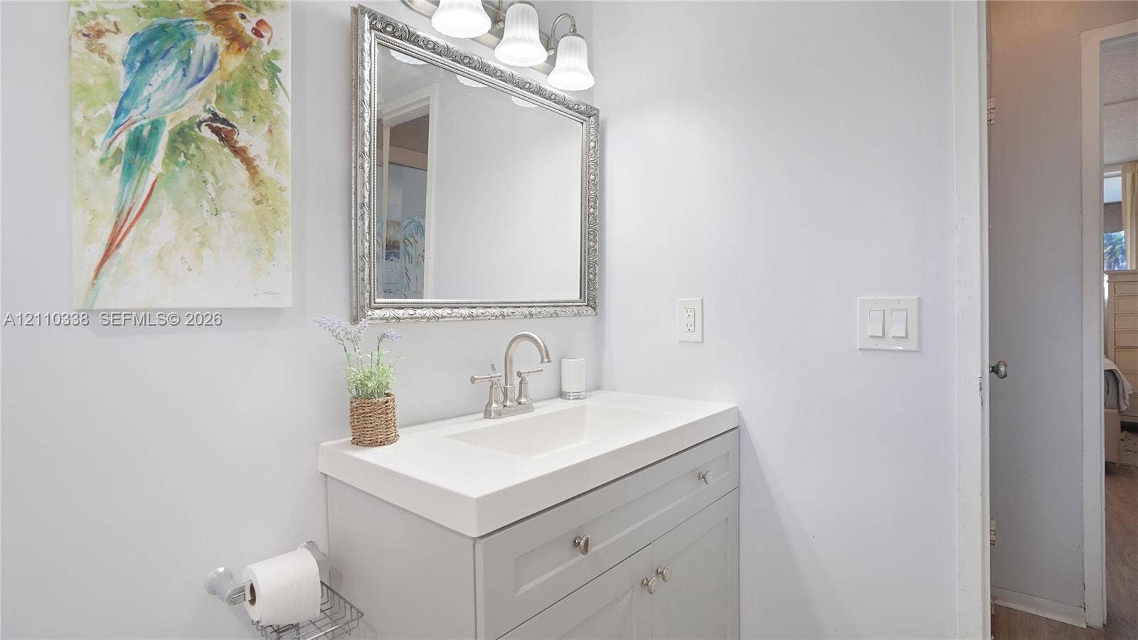 Gray vanity with integrated rectangular sink and polished nickel faucet, topped by a framed rectangular wall mirror and a three-light vanity fixture