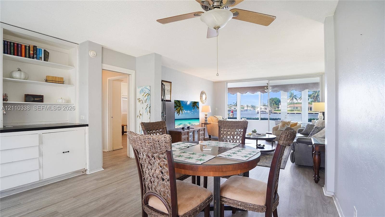 Living area featuring wood-finish flooring, floor-to-ceiling glass sliding doors, built-in shelving, white cabinetry with a stone-top surface, and a central ceiling fan