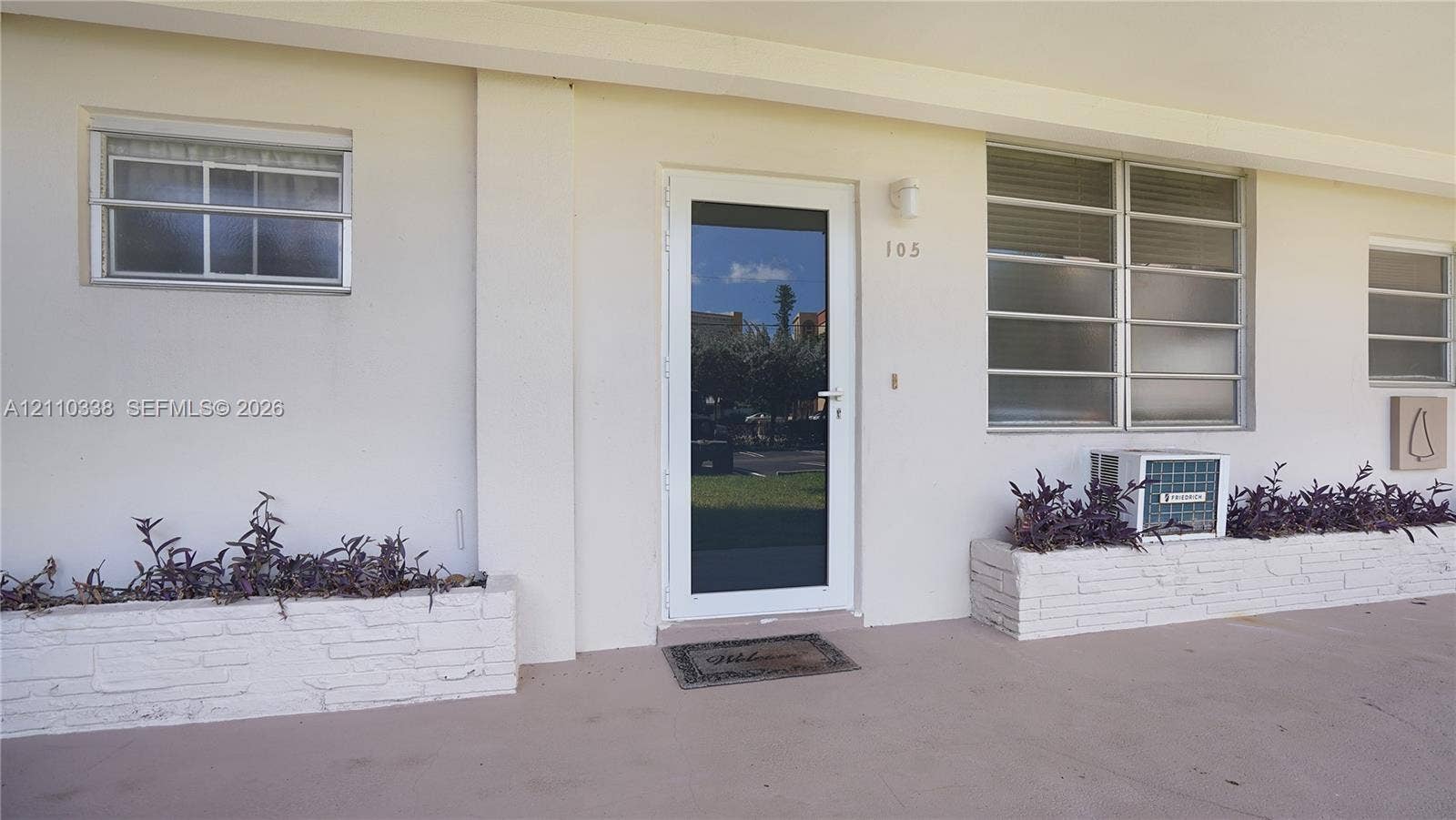 Exterior entrance featuring a white-framed glass door, horizontal-pane windows, and integrated brick-faced planters