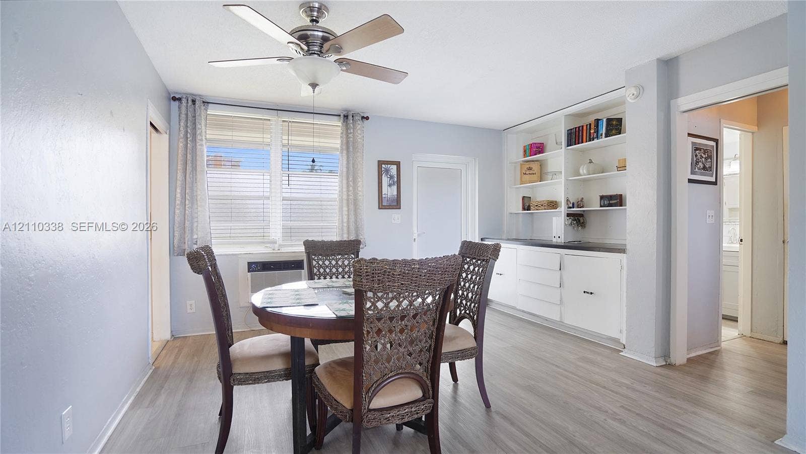 Dining area featuring wood-finish flooring, built-in white cabinetry with open shelving, and a central ceiling fan