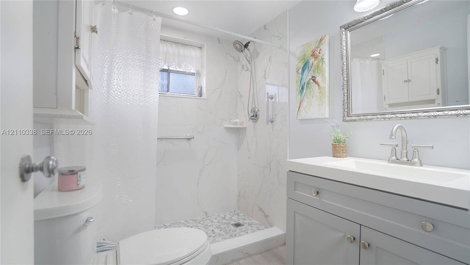 Walk-in shower with stone-finish surround and integrated shelving, grey vanity with rectangular basin, brushed-nickel widespread faucet, and rectangular mirror