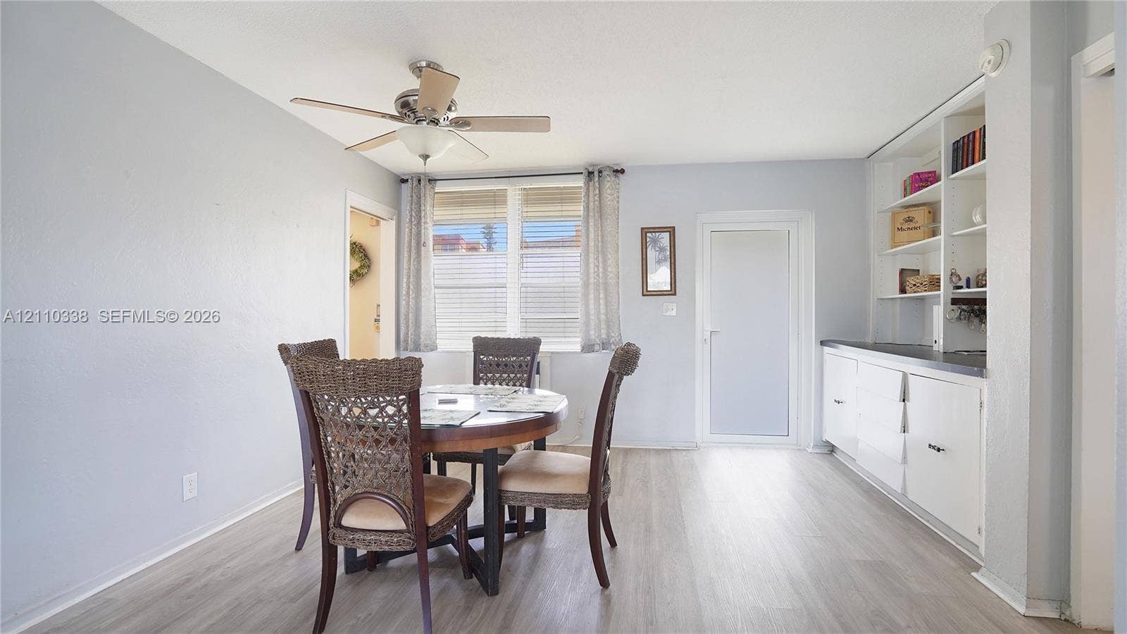 Interior space featuring light-toned wood-finish flooring, built-in floor-to-ceiling cabinetry with shelving, a ceiling fan with integrated lighting, and multi-pane windows