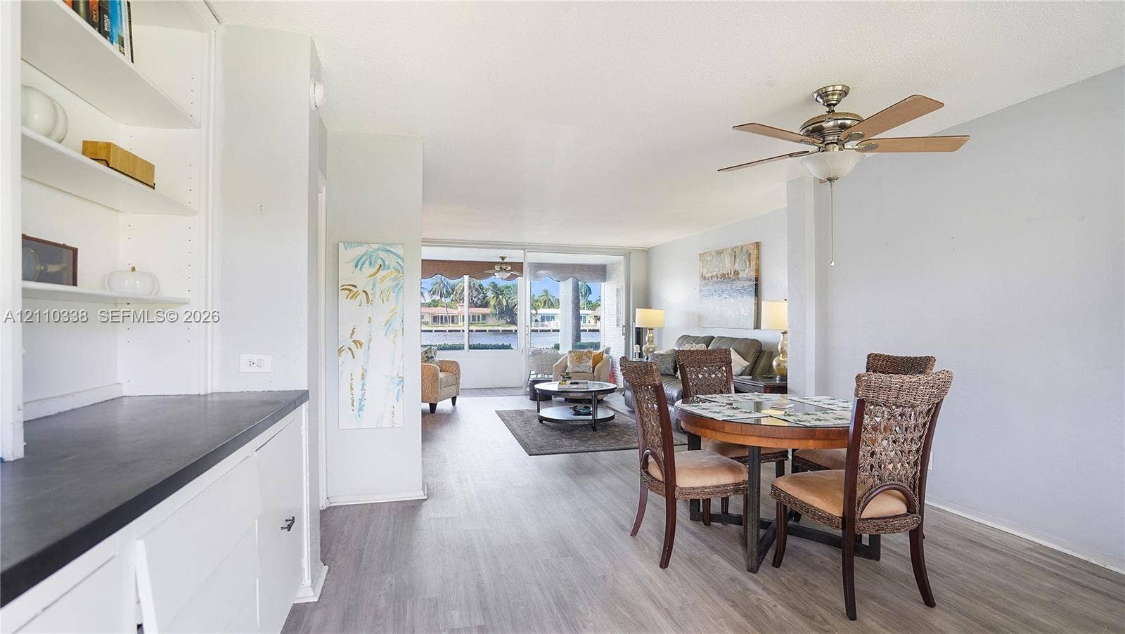 Open-concept floor plan featuring wood-finish flooring, built-in cabinetry with a dark countertop, a ceiling fan, and floor-to-ceiling windows
