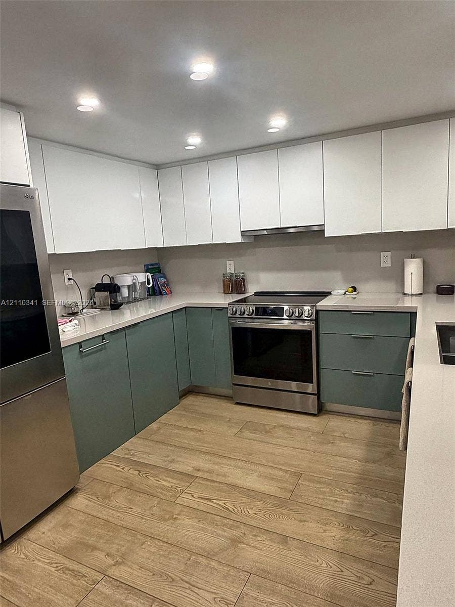 Kitchen featuring two-tone cabinetry with matte white upper and sage green lower units, light-toned stone-finish countertops, stainless steel appliances, and wood-finish plank flooring