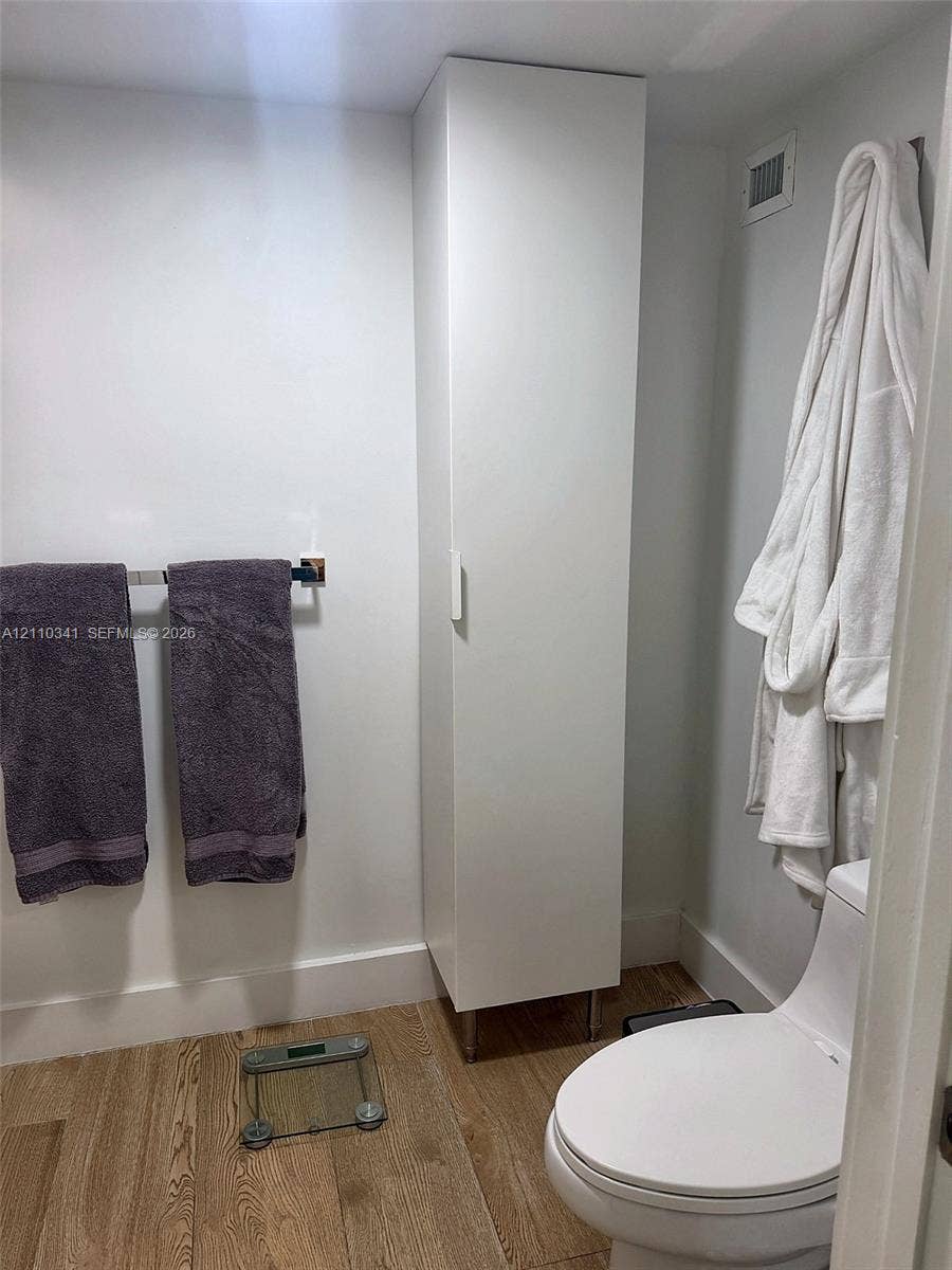 Full-height white storage cabinetry, wood-finish flooring, and a contemporary white toilet