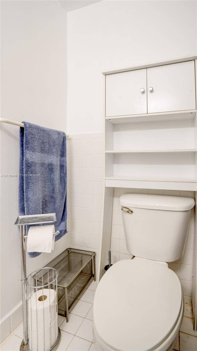 8600 SW 67th Avenue, #905, Pinecrest, Pinecrest, FL 33156 White tile wall surround, porcelain commode, and built-in white over-the-toilet storage unit featuring dual cabinet doors and open shelving