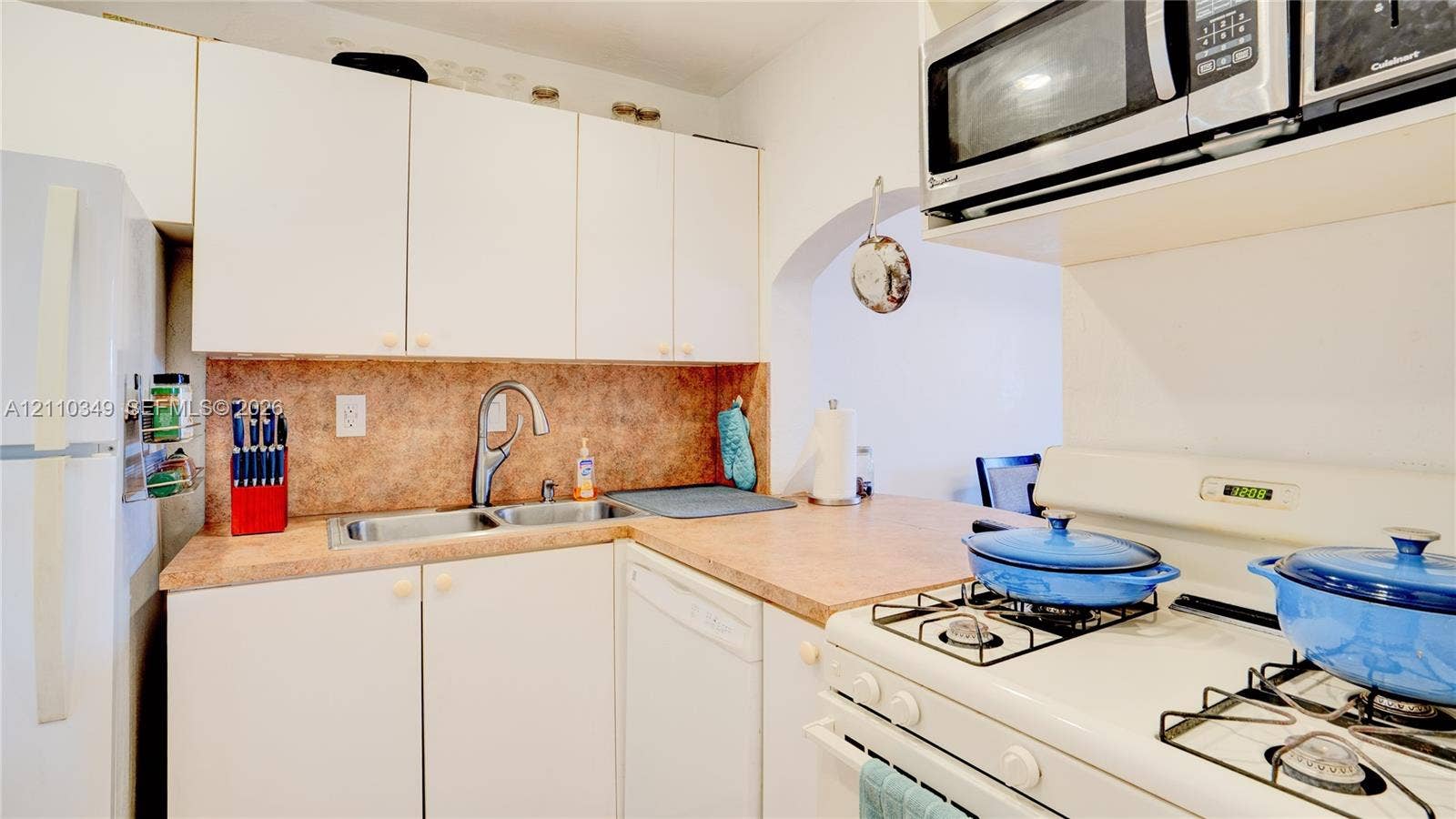 8600 SW 67th Avenue, #905, Pinecrest, Pinecrest, FL 33156 Kitchen featuring white cabinetry, solid-surface countertops, dual-basin stainless steel sink with high-arch faucet, built-in stainless steel microwave, and gas range