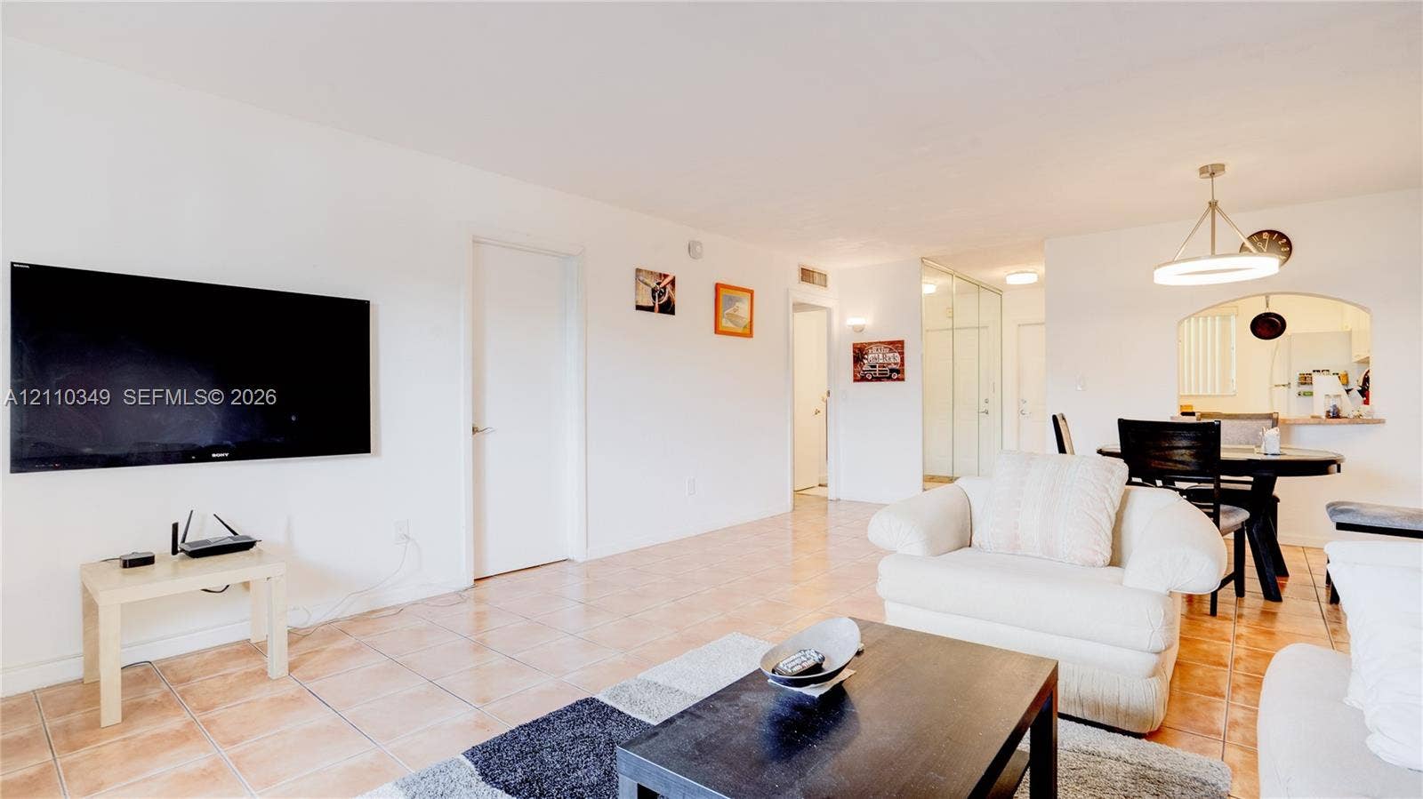 8600 SW 67th Avenue, #905, Pinecrest, Pinecrest, FL 33156 Open-concept interior featuring light-toned tile flooring, recessed ceiling lighting, a contemporary circular metal chandelier, and an arched wall opening with a built-in counter
