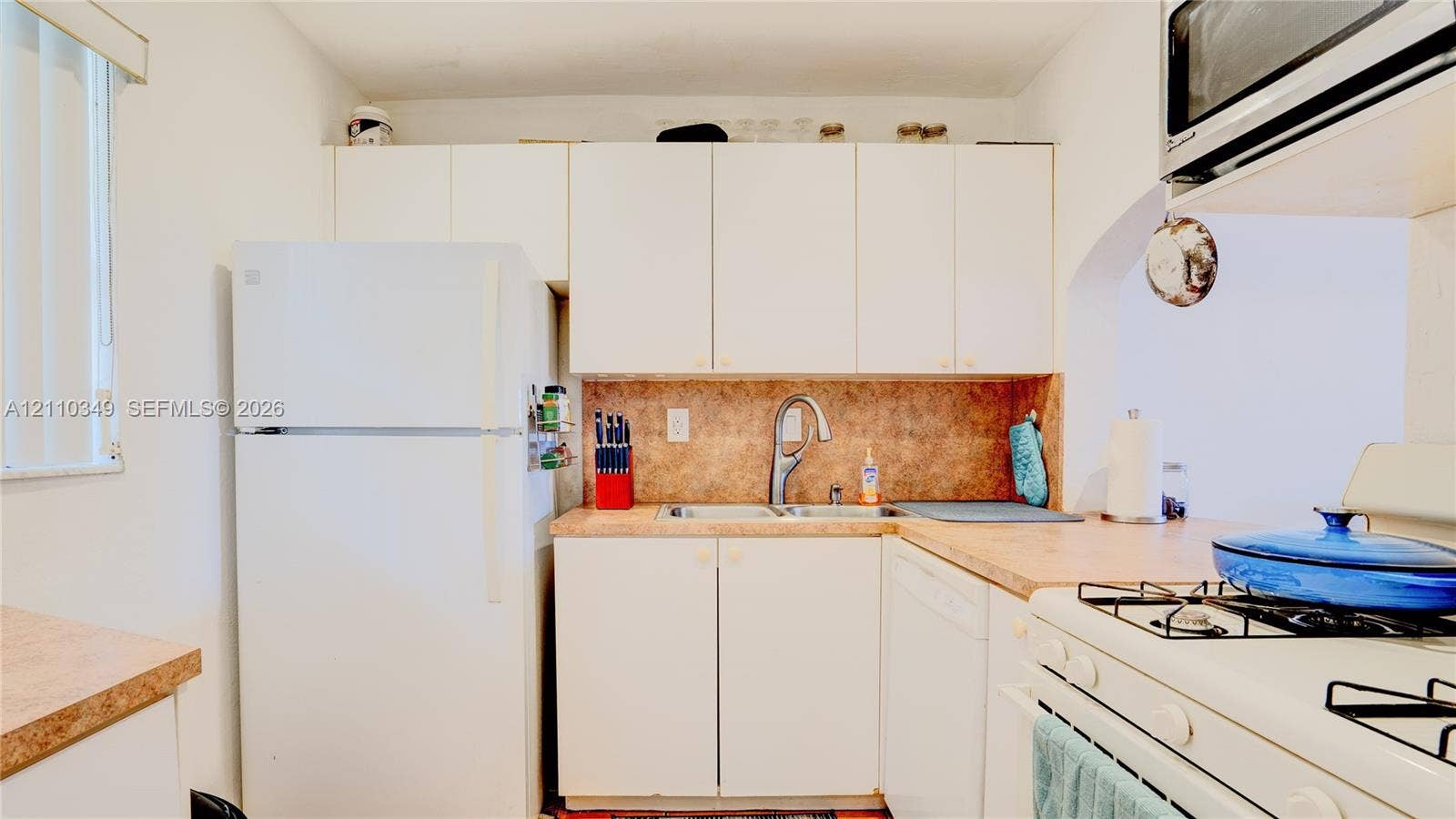 8600 SW 67th Avenue, #905, Pinecrest, Pinecrest, FL 33156 Kitchen featuring white cabinetry, solid-surface countertops, dual-basin stainless steel sink with high-arc faucet, and white appliances including a built-in microwave and gas range