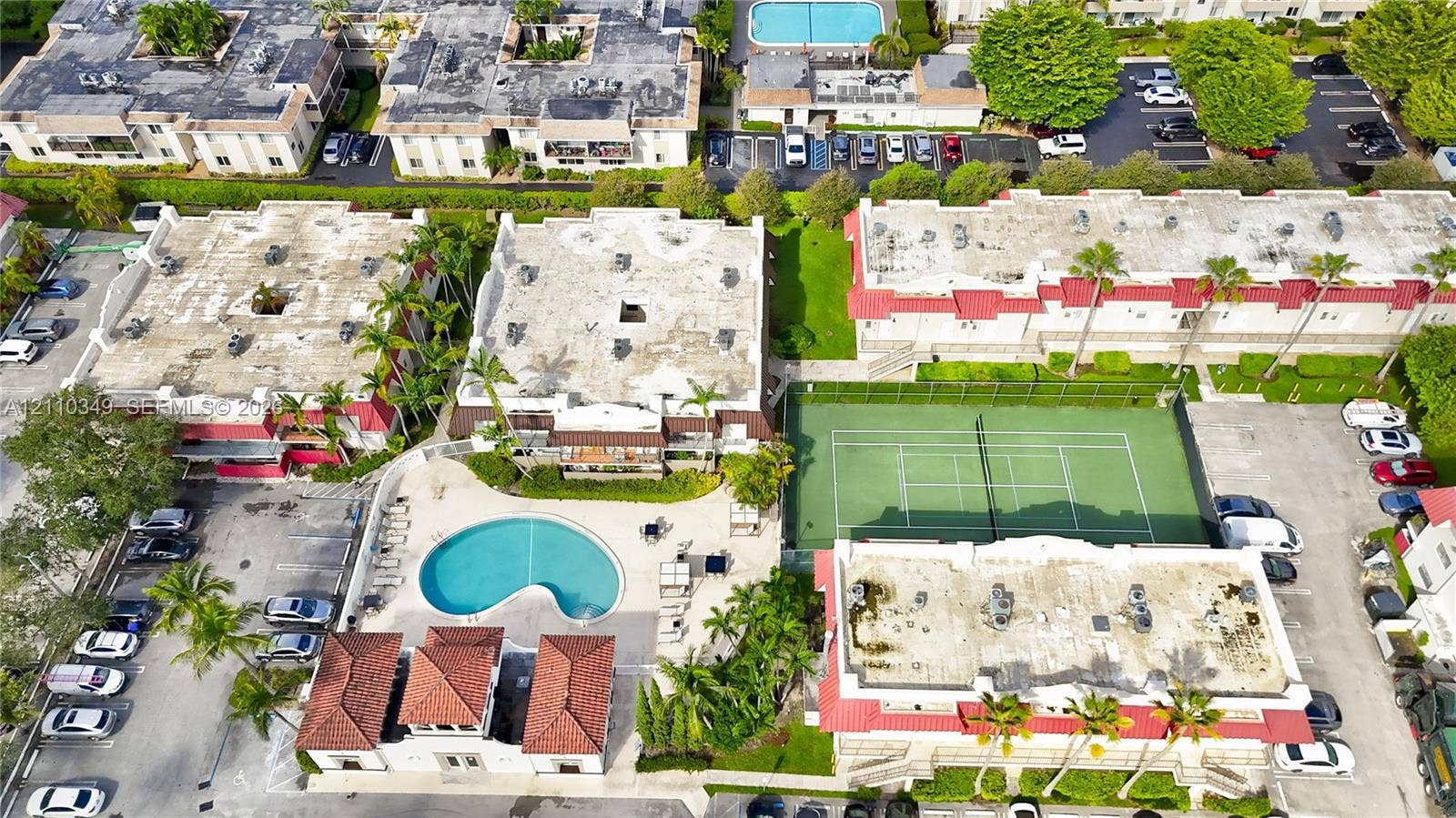 8600 SW 67th Avenue, #905, Pinecrest, Pinecrest, FL 33156 Aerial perspective of community grounds featuring a swimming pool, tennis court, tiled roof structures, and paved parking areas