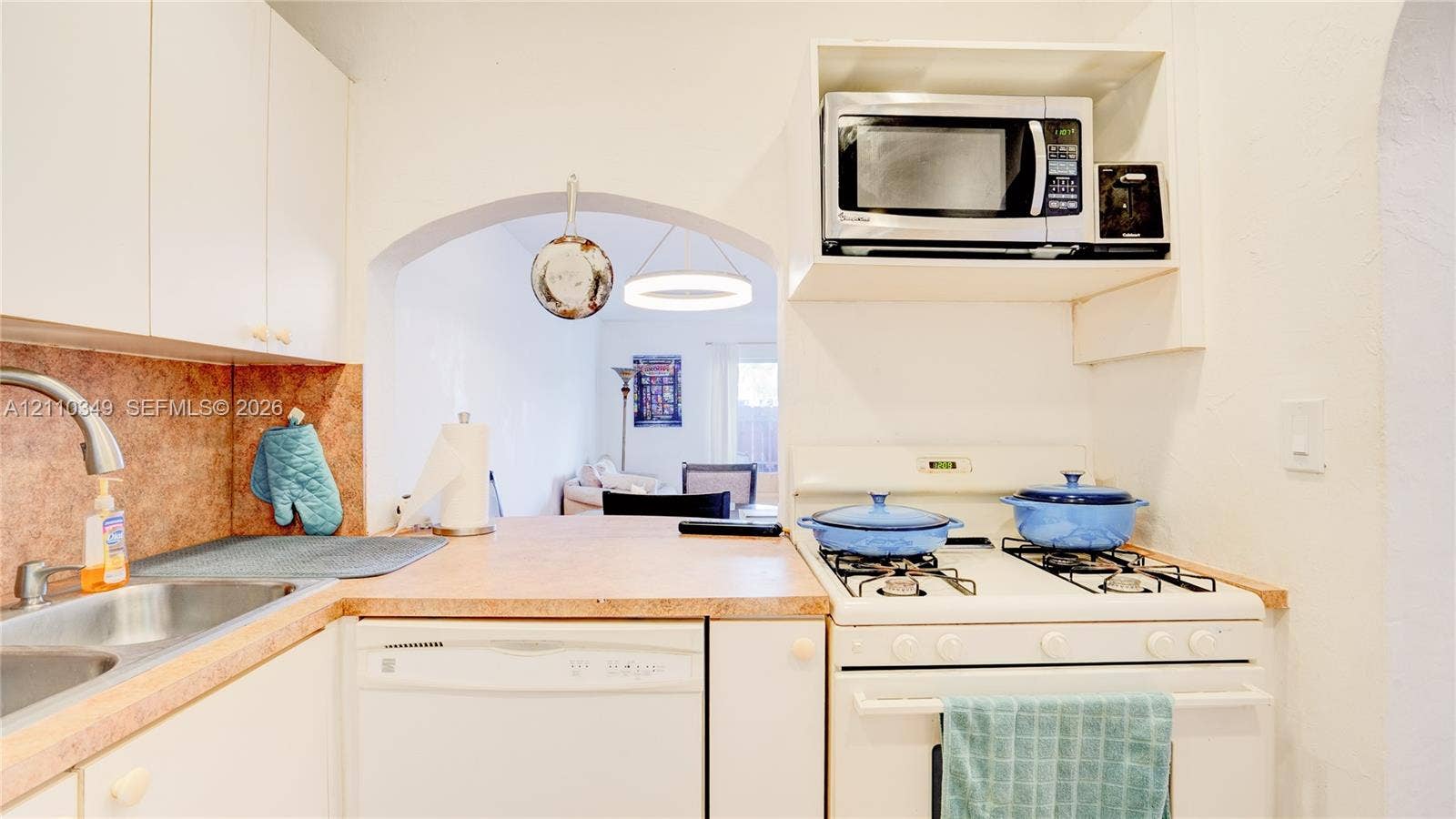 8600 SW 67th Avenue, #905, Pinecrest, Pinecrest, FL 33156 Kitchen featuring white cabinetry, an integrated gas range with overhead microwave, a stainless steel sink with a pull-down faucet, and an arched entryway