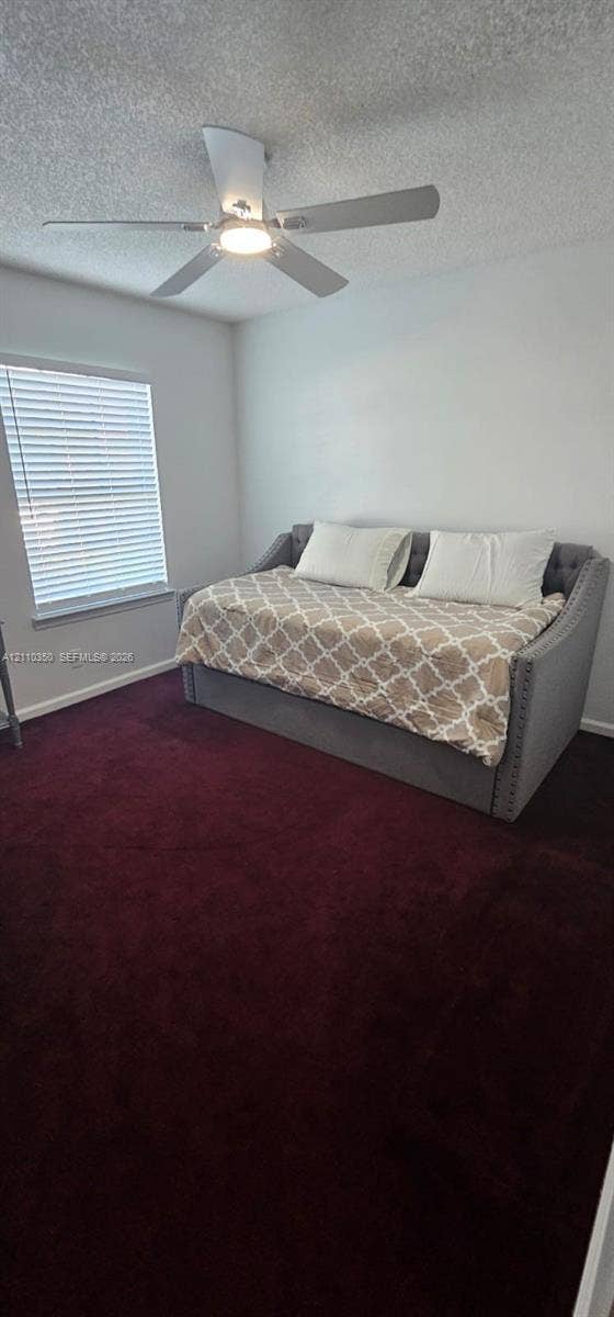 Room featuring plush carpeting, a multi-blade ceiling fan with integrated lighting, and a single-hung window with horizontal blinds