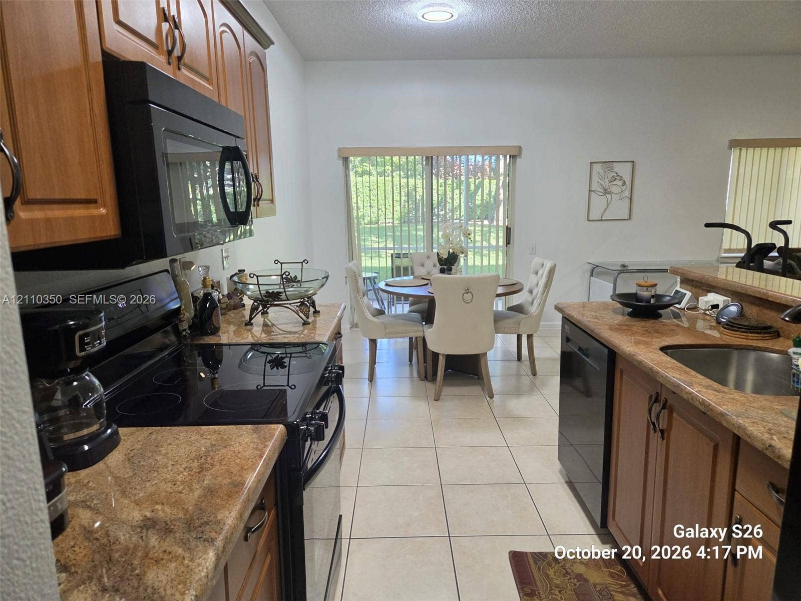 Kitchen featuring wood cabinetry, solid surface countertops, a black appliance suite, tile flooring, and a sliding glass door