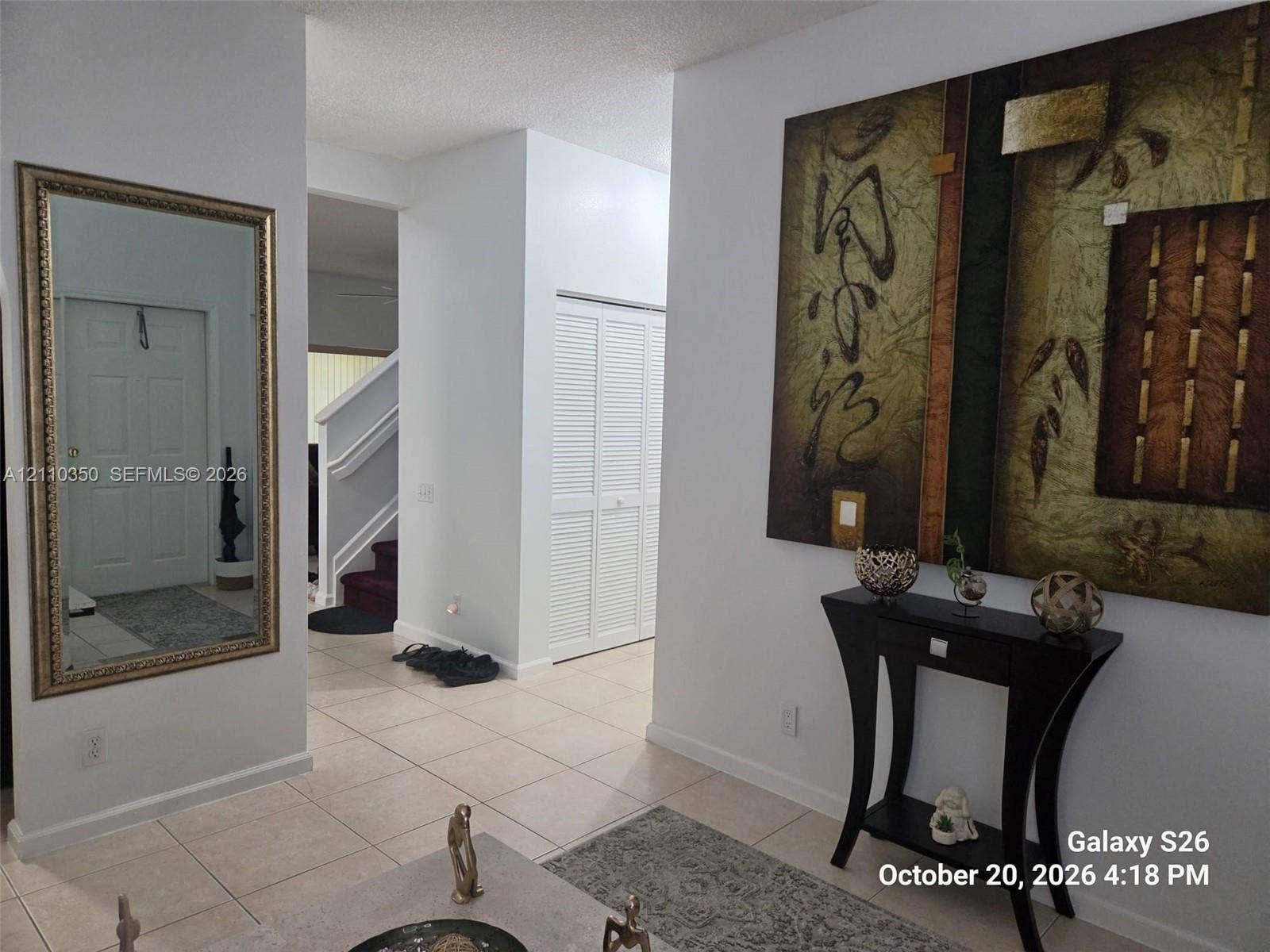 Foyer featuring neutral tile flooring, white wall-mounted louvered closet doors, and a wall-mounted decorative mirror