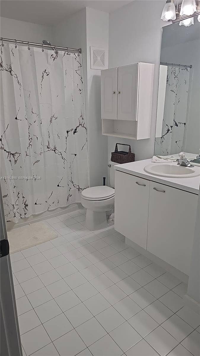 Bathroom featuring white ceramic tile flooring, vanity with an integrated basin, wall-mounted storage cabinetry, and a full-length mirror