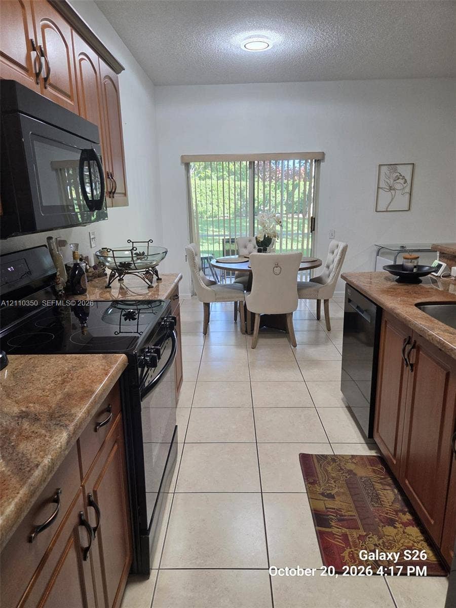 Kitchen featuring wood-finish cabinetry, stone-finish countertops, black built-in appliances, ceramic tile flooring, and a sliding glass door