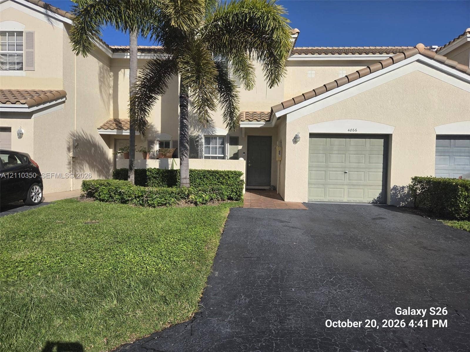 Stucco exterior featuring a tiled roof, attached single-car garage, paved driveway, and mature landscaping