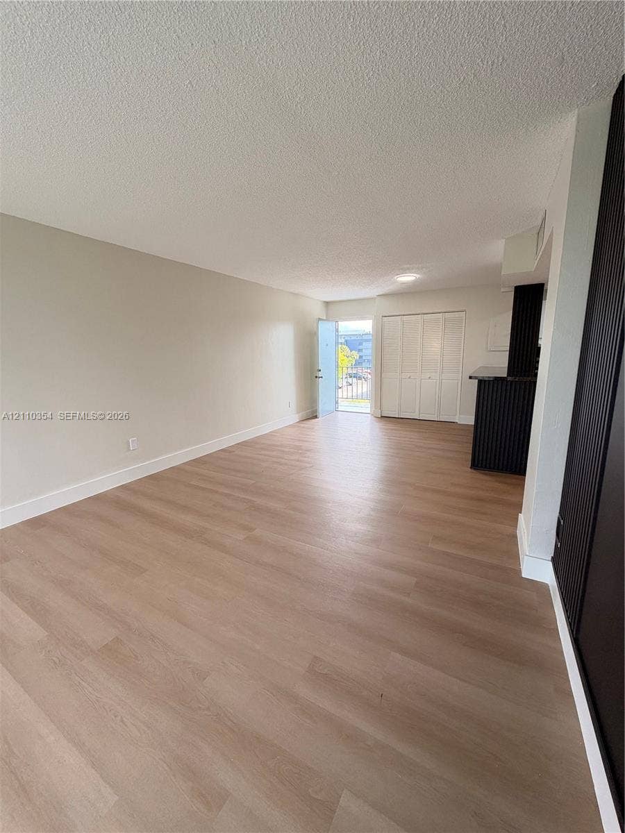 8801 W Flagler Street, #309, Miami, Miami, FL 33174 Open-concept living space featuring wood-finish flooring, neutral wall paint, floor-to-ceiling built-in closet cabinetry, and a dark-toned breakfast bar
