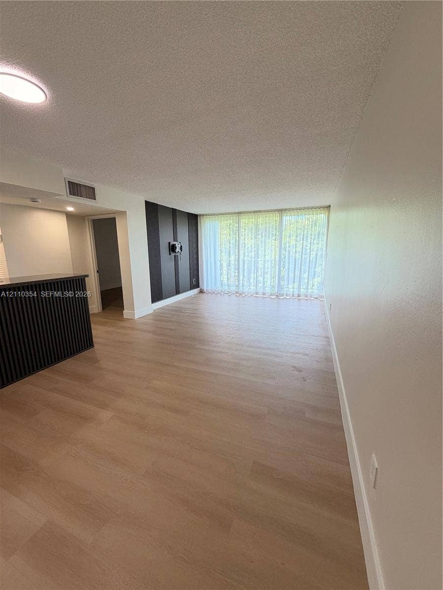 8801 W Flagler Street, #309, Miami, Miami, FL 33174 Open-concept living space featuring wood-finish flooring, floor-to-ceiling glass wall, accent wall with vertical paneling, and a kitchen peninsula with integrated vertical slat detailing