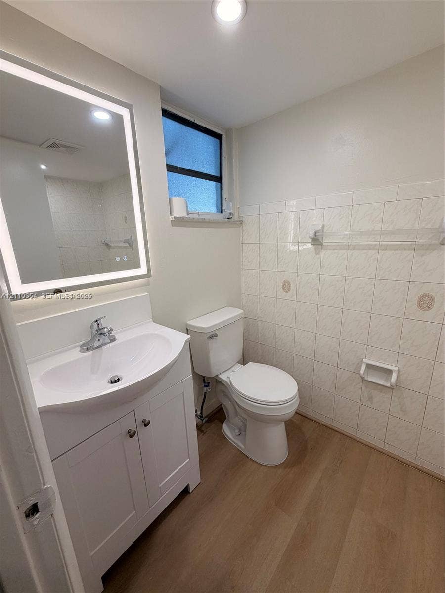 8801 W Flagler Street, #309, Miami, Miami, FL 33174 Bathroom featuring a vanity cabinet with a stone-top integrated sink, LED-backlit mirror, wood-finish flooring, and wall-mounted ceramic tiling