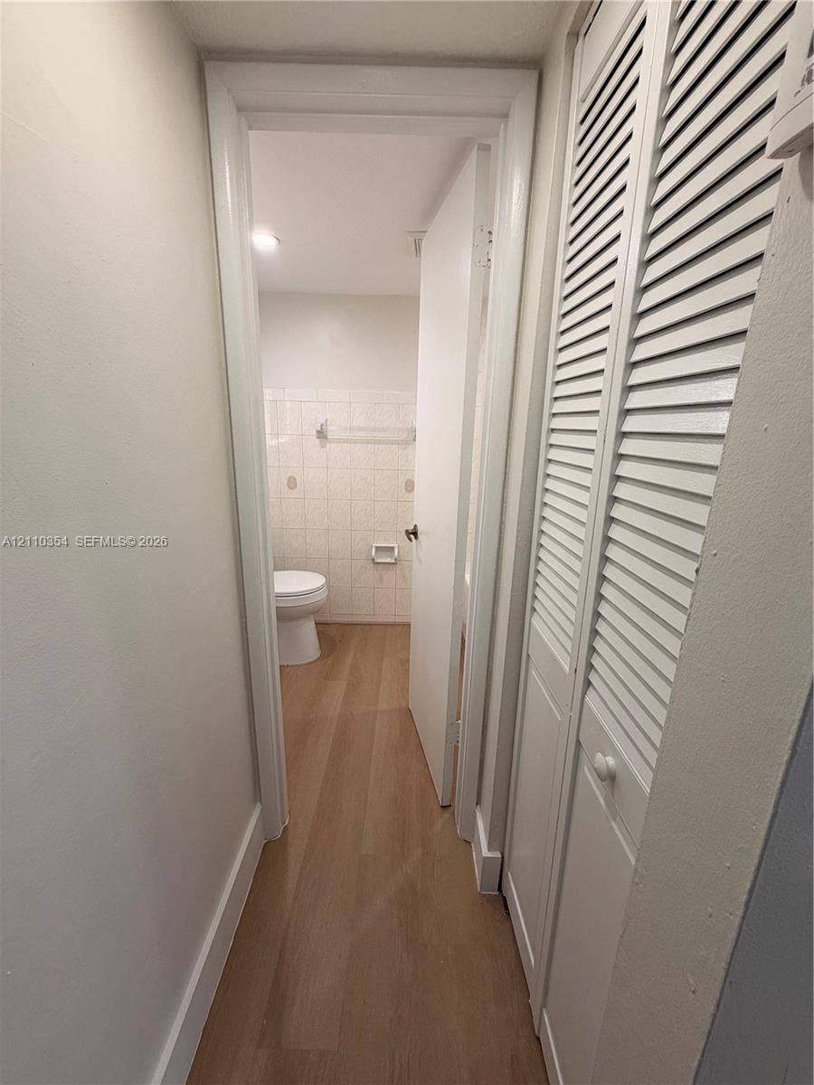 8801 W Flagler Street, #309, Miami, Miami, FL 33174 Hallway featuring wood-finish flooring and white louvered-door closets, leading to a space with tile-surround walls