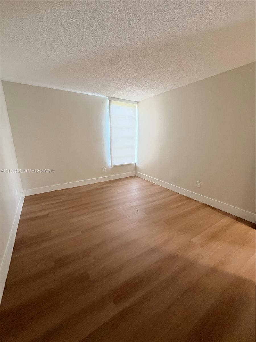 8801 W Flagler Street, #309, Miami, Miami, FL 33174 Neutral-toned walls, wood-finish flooring, and natural light entry through a vertical window with a roller shade