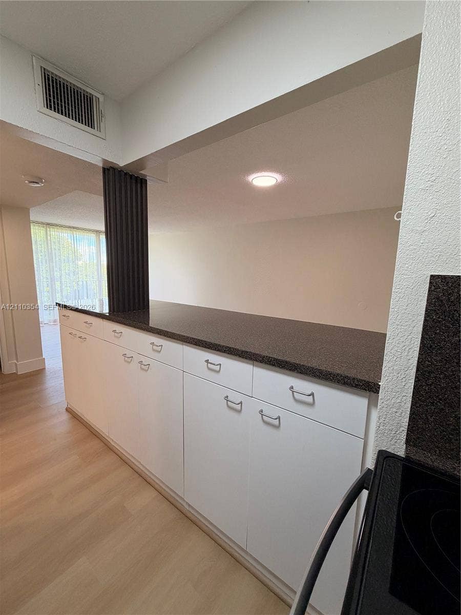 8801 W Flagler Street, #309, Miami, Miami, FL 33174 Kitchen pass-through featuring a dark stone-finish countertop, white cabinetry with silver-tone hardware, and wood-finish flooring