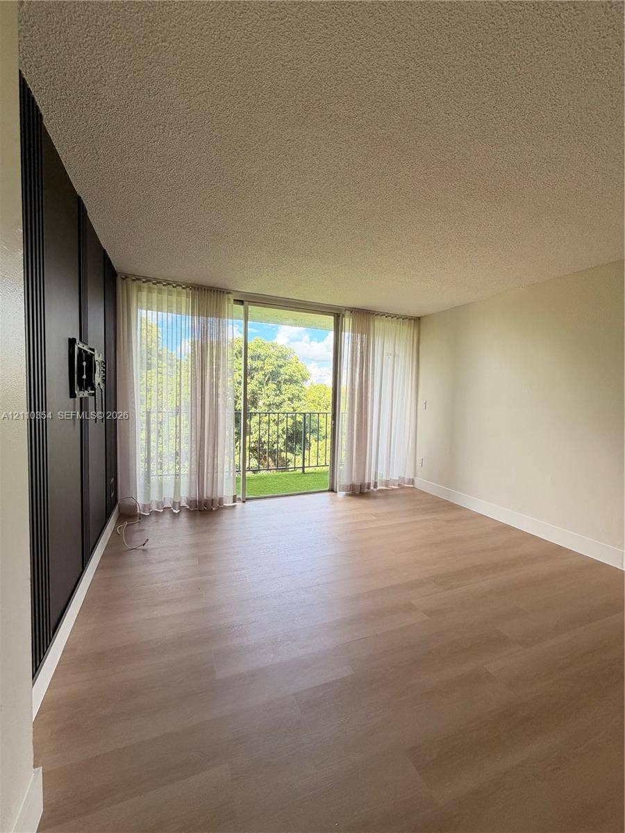 8801 W Flagler Street, #309, Miami, Miami, FL 33174 Wood-finish flooring, floor-to-ceiling sliding glass doors, decorative dark vertical paneling, and a metal-railed exterior balcony