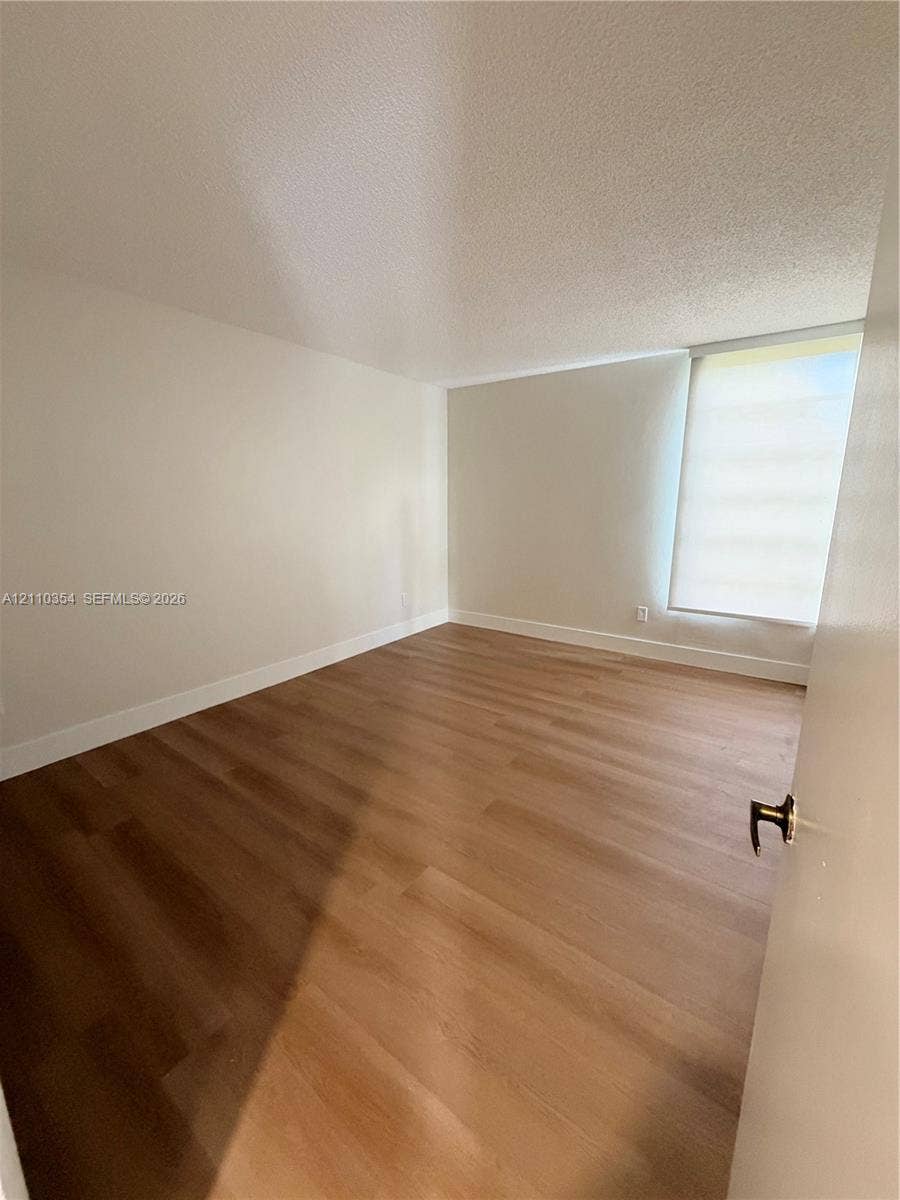 8801 W Flagler Street, #309, Miami, Miami, FL 33174 Room featuring neutral wall finishes, wood-finish flooring, and a window with a retractable shade