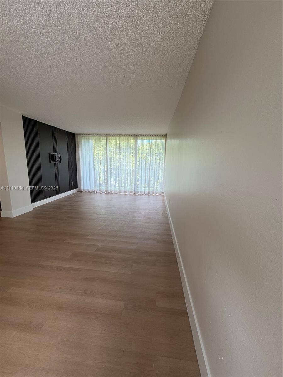 8801 W Flagler Street, #309, Miami, Miami, FL 33174 Living area featuring wood-finish flooring, floor-to-ceiling windows, and a dark-toned vertical accent wall