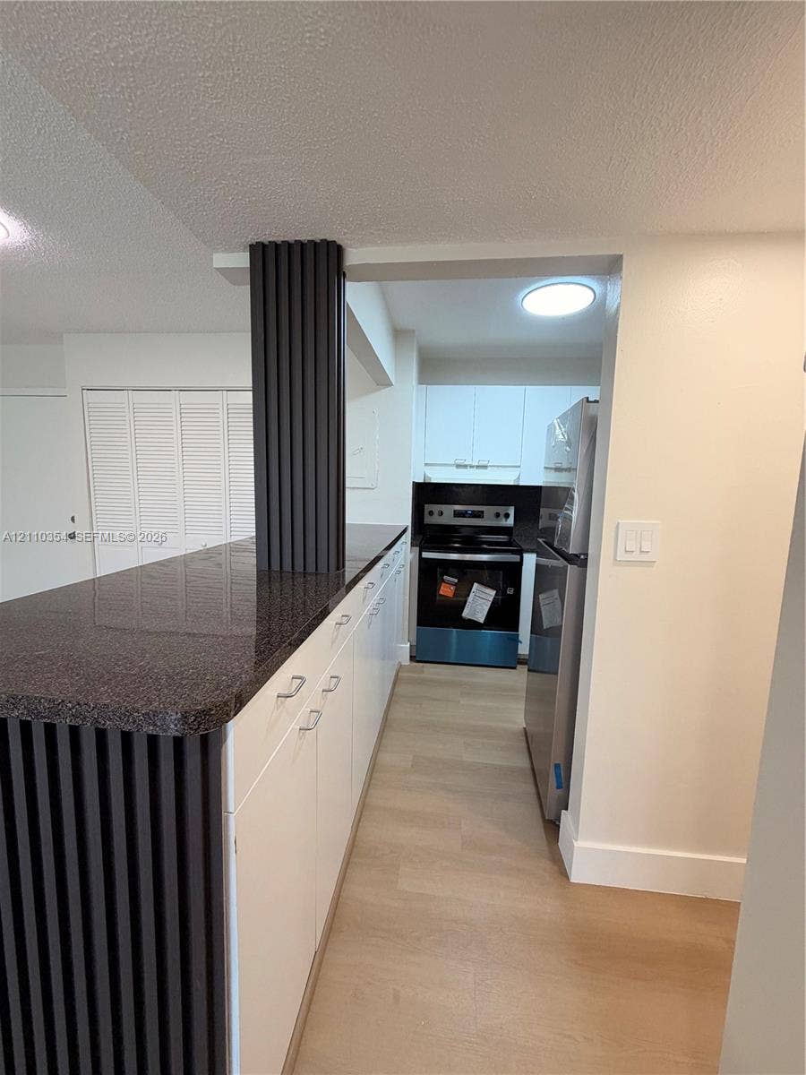 8801 W Flagler Street, #309, Miami, Miami, FL 33174 Kitchen featuring white cabinetry, dark stone-finish countertops, wood-finish flooring, and a decorative slatted support pillar