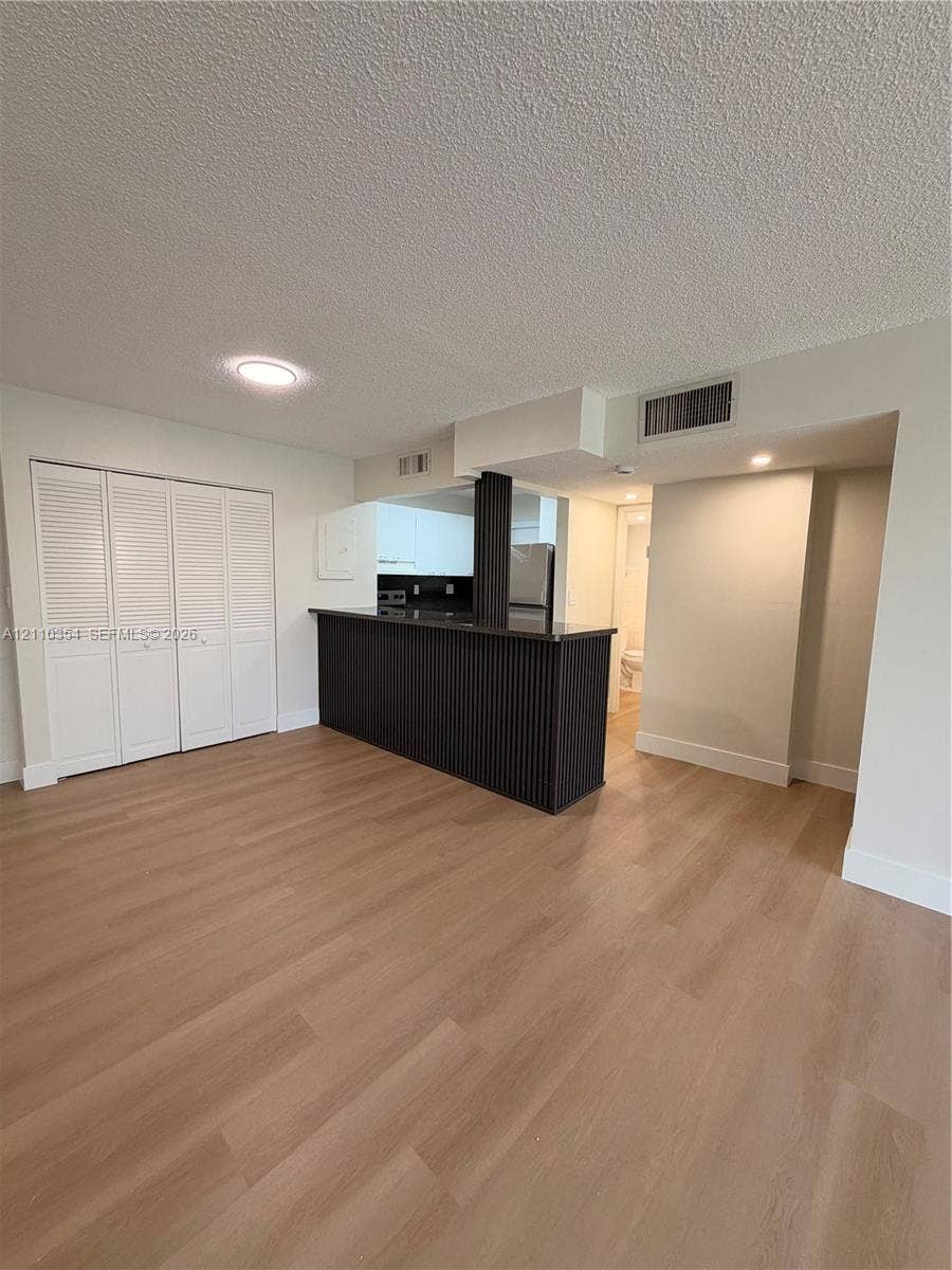 8801 W Flagler Street, #309, Miami, Miami, FL 33174 Wood-finish flooring, white louvered-door closet, and dark-toned breakfast bar featuring fluted cabinetry detailing