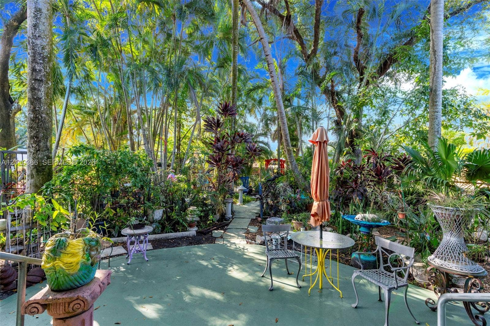 2361 SW 18th Avenue, Fort Lauderdale, FL 33315 Rear outdoor patio featuring a concrete surface and natural stone paver pathway surrounded by mature trees and lush tropical vegetation