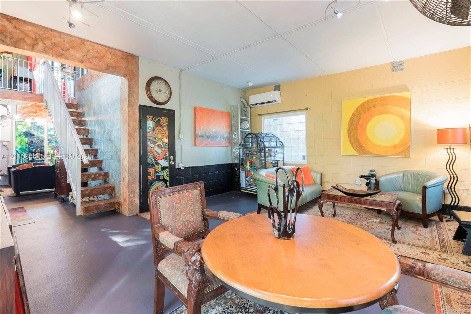 2361 SW 18th Avenue, Fort Lauderdale, FL 33315 Open-concept interior featuring a structural timber beam, painted masonry walls, staircase with metal railing, wall-mounted air conditioning unit, and decorative glass-paneled door