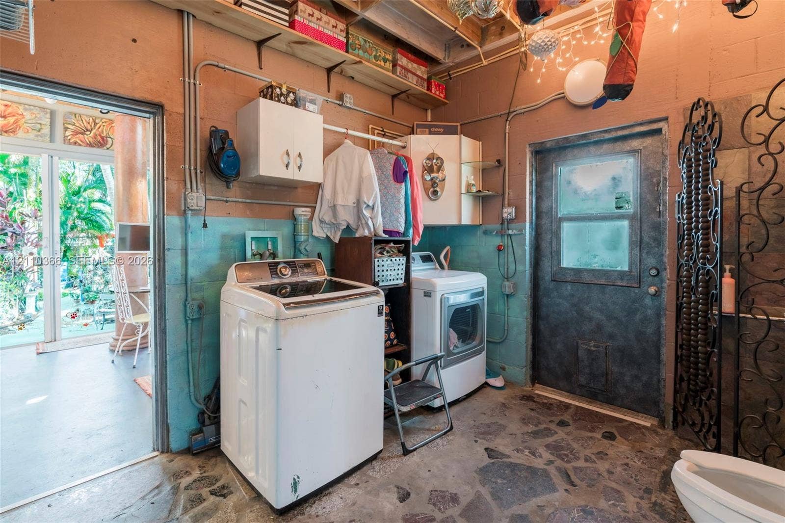 2361 SW 18th Avenue, Fort Lauderdale, FL 33315 Utility room featuring slate-patterned stone flooring, dual-tone painted masonry walls, integrated wall-mounted storage cabinetry, and a glass-paneled exterior entry door