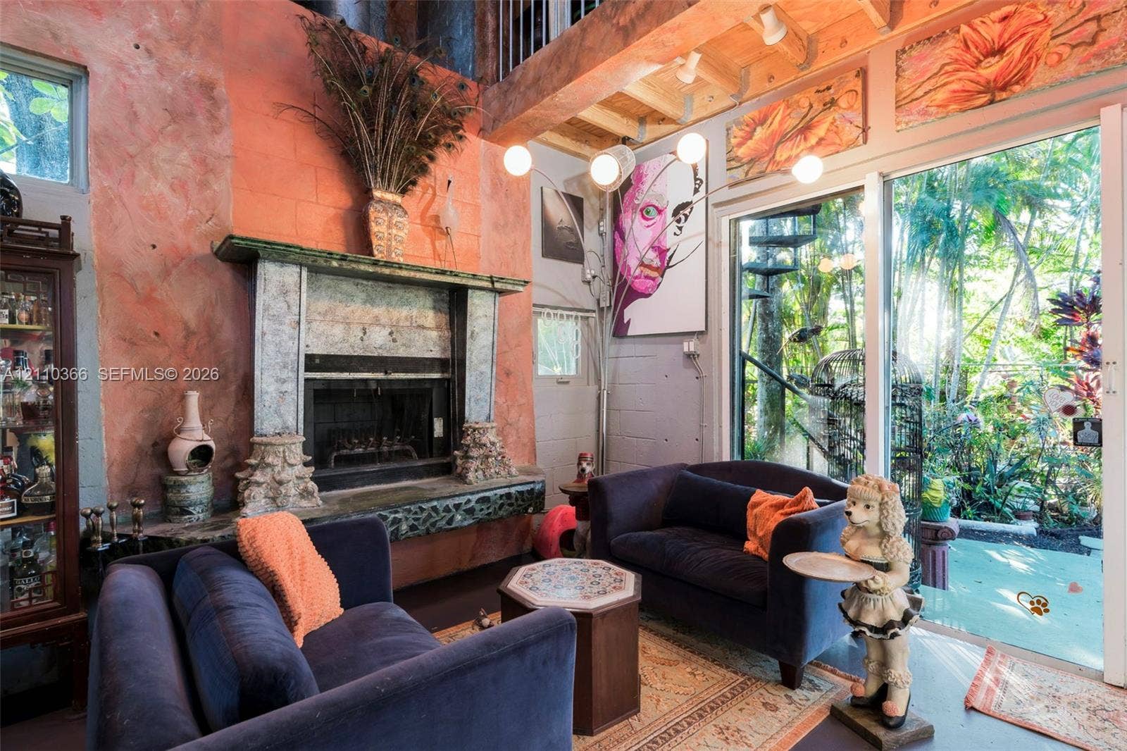 2361 SW 18th Avenue, Fort Lauderdale, FL 33315 Double-height living area featuring an exposed wood-beam ceiling, textured coral-toned wall, fireplace with an ornate stone mantel, and floor-to-ceiling glass sliding doors