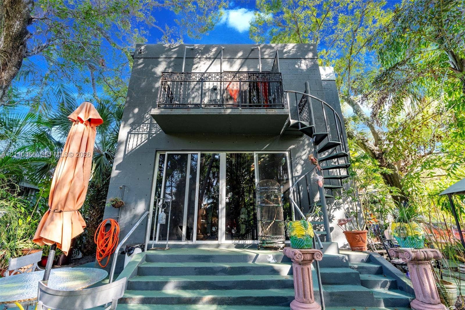 2361 SW 18th Avenue, Fort Lauderdale, FL 33315 Multi-level exterior featuring a painted masonry facade, second-story balcony with decorative metal railing, exterior spiral staircase, and full-height glass sliding doors opening to a concrete staircase