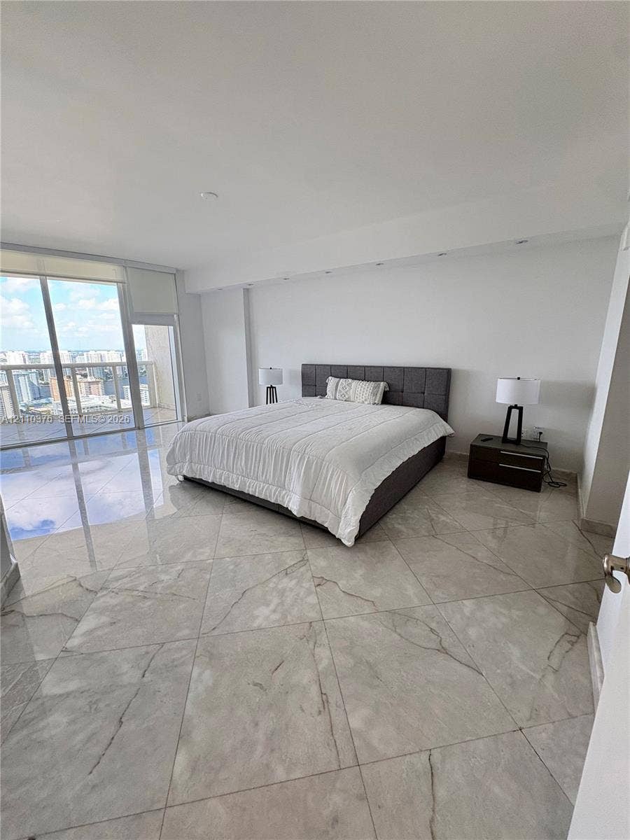 Floor-to-ceiling glass sliding doors, large-format polished tile flooring, recessed ceiling lighting, and a private balcony