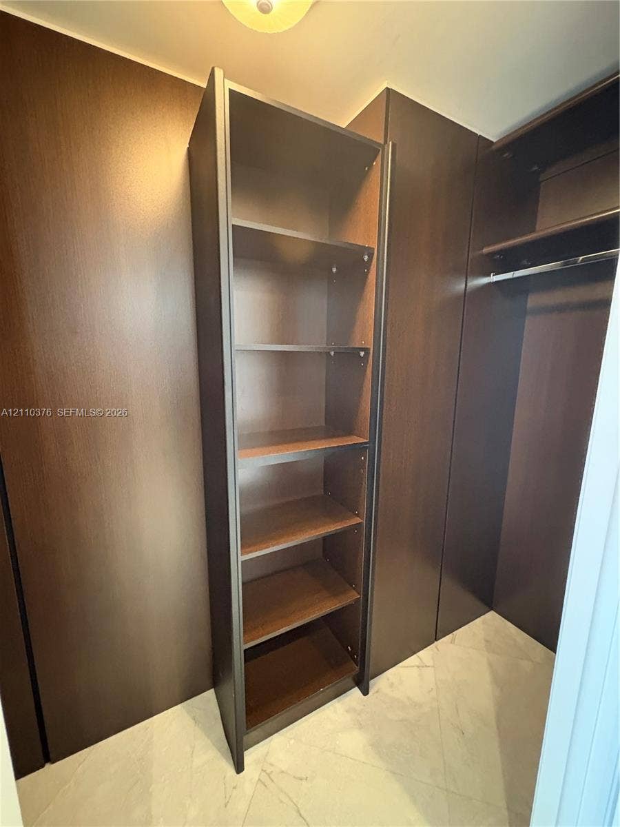 Built-in storage system featuring dark wood-finish cabinetry, adjustable shelving, integrated hanging rods, and large-format tile flooring
