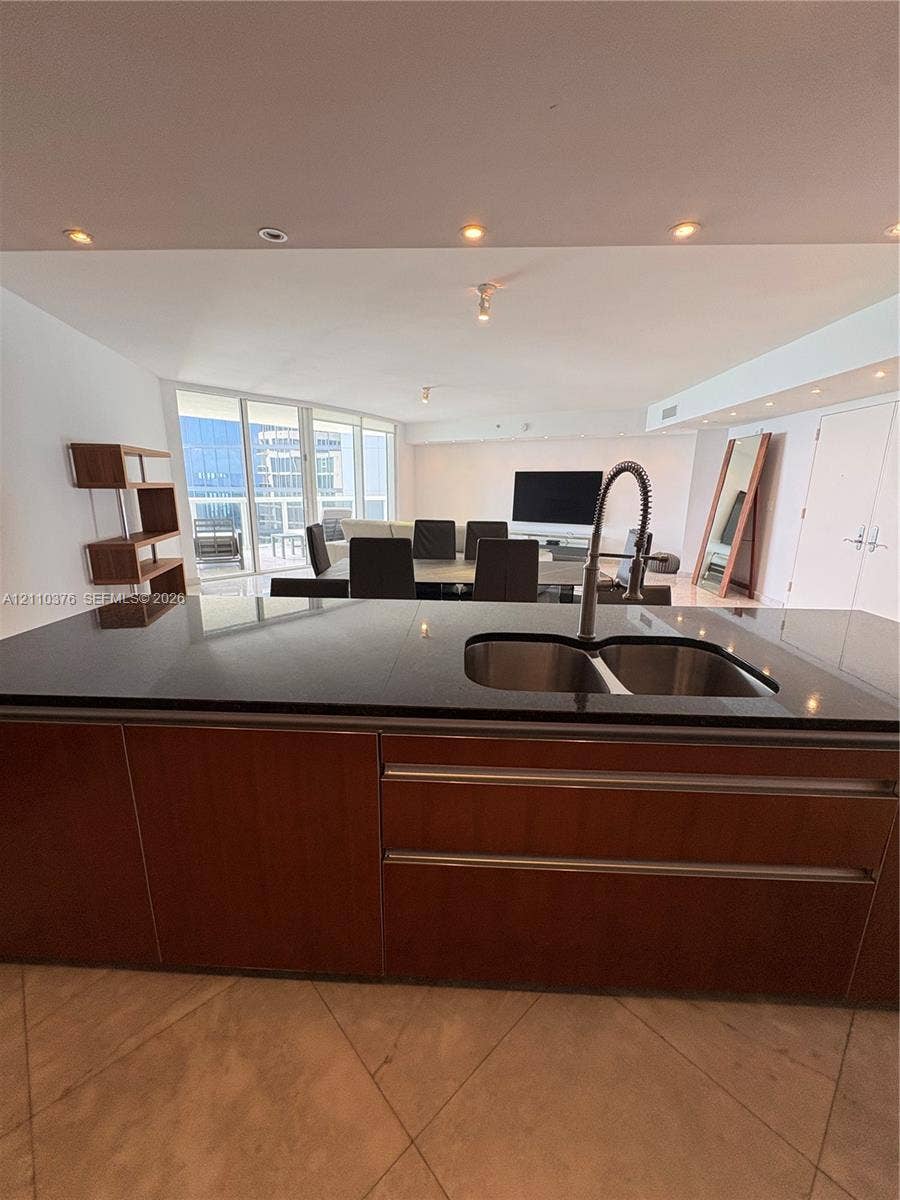 Kitchen island featuring dark-toned solid surfacing, stainless steel double-basin undermount sink, gooseneck faucet, and wood-finish cabinetry