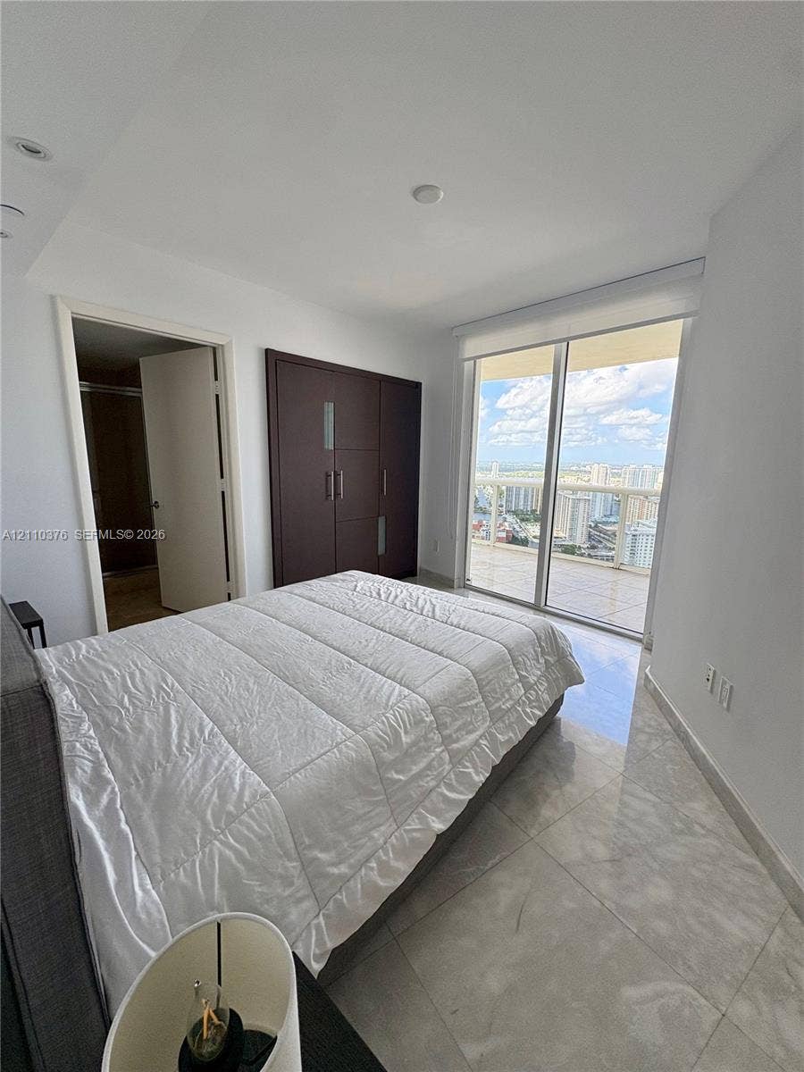 Large-format tile flooring, built-in dark wood-finish cabinetry, recessed ceiling lighting, and floor-to-ceiling glass sliding doors opening to an exterior balcony