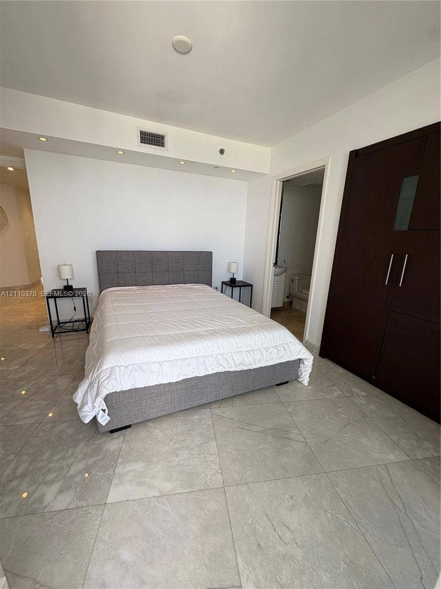 Large-format light-toned tile flooring, recessed ceiling lighting, and built-in dark wood-finish cabinetry